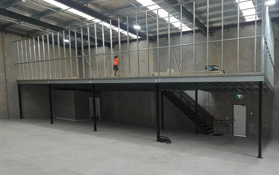 Completed mezzanine floor on steel columns in a warehouse, with the access stair and edge guardrail in